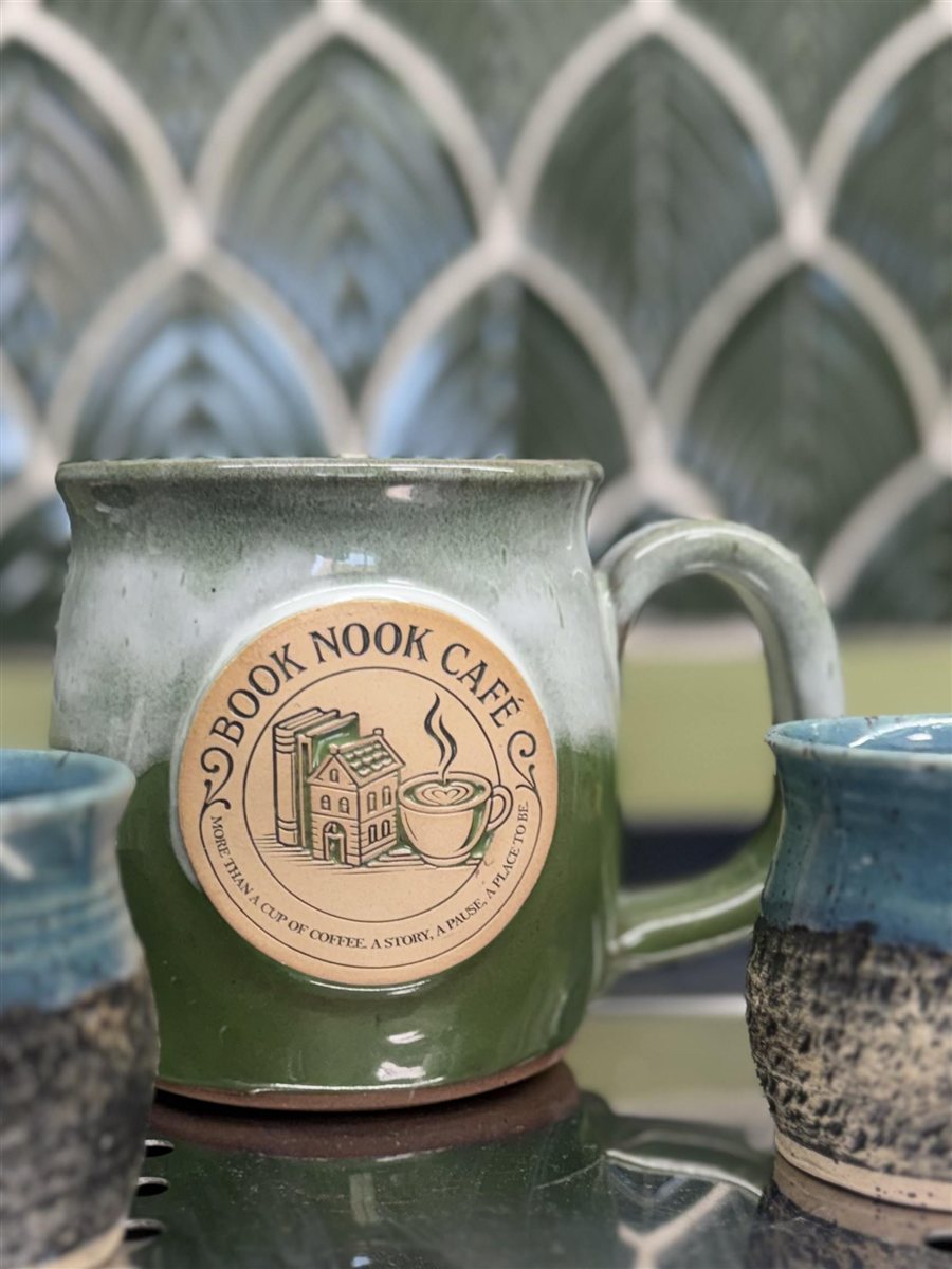Green ceramic Book Nook Cafe mug with the cafe logo, between two blue cups.
